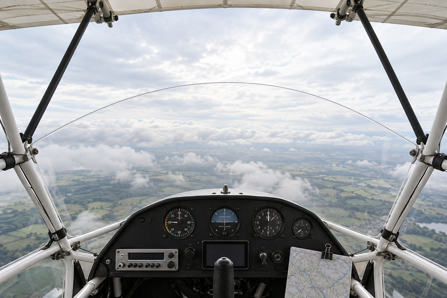 Vista de dentro de um avião ultraleve, com estrutura tubular, asa alta e um painel compacto sobre uma paisagem de nuvens.